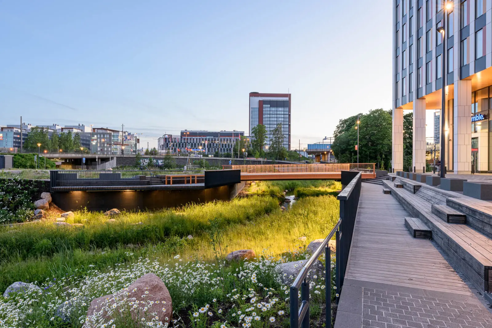 Blue-green infrastructure landscape combining ecological stormwater management, biodiverse planting, pedestrian connectivity, and public gathering spaces within a dense urban environment.